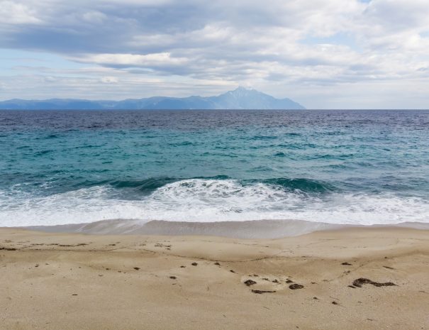 A beach with blue waves of the Aegean sea and mountain on the background, Greece